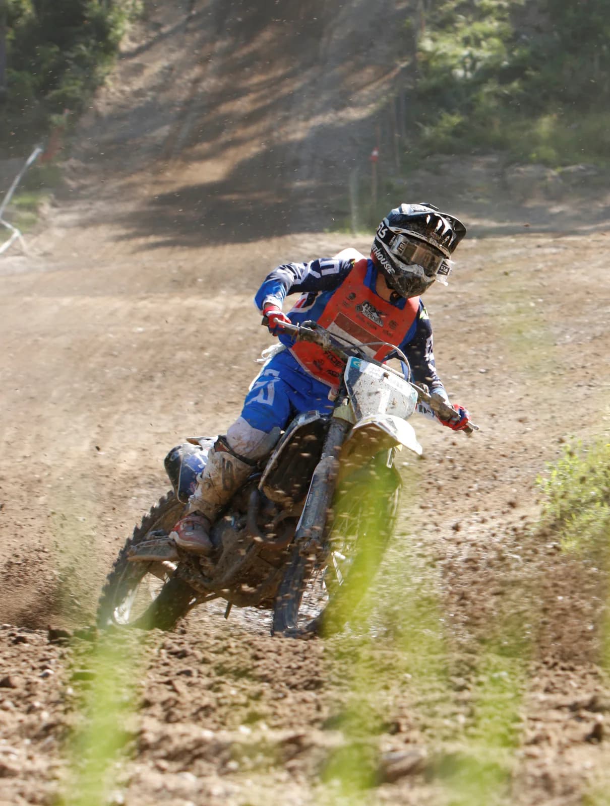 Motocross bike leaned into a turn, rear wheel throwing dirt.
